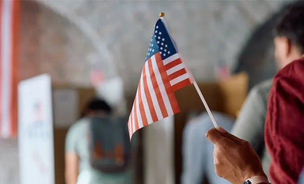 A voter holding up an American flag while waiting in line to vote