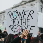 Photo of a demonstrator holding up a sign that reads "Power to the People"