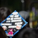 Closeup of a graduation cap that reads "Paving the way for my familia and comunidad. Educated mujer first gen"