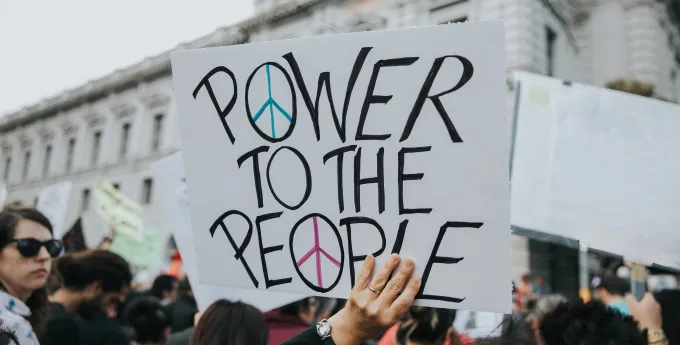 Photo of a demonstrator holding up a sign that reads "Power to the People"