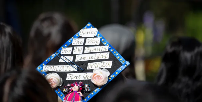 Closeup of a graduation cap that reads "Paving the way for my familia and comunidad. Educated mujer first gen"